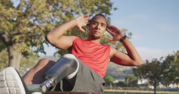 一个有假腿的残疾混血儿的侧视图 在公园里锻炼 做仰卧起坐 用耳机听音乐 动作缓慢 — 图库视频影像