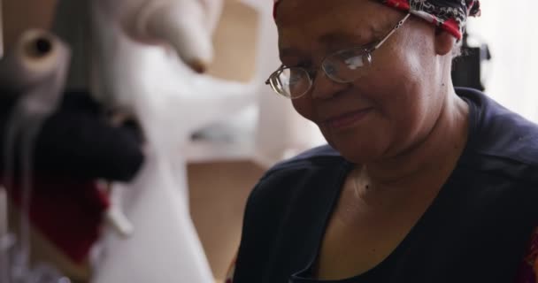 Vue latérale rapprochée d'une femme métissée portant un tablier à l'aide d'un smartphone et souriant dans l'atelier d'une usine de chapeaux, avec des matériaux et des équipements en arrière-plan, au ralenti 