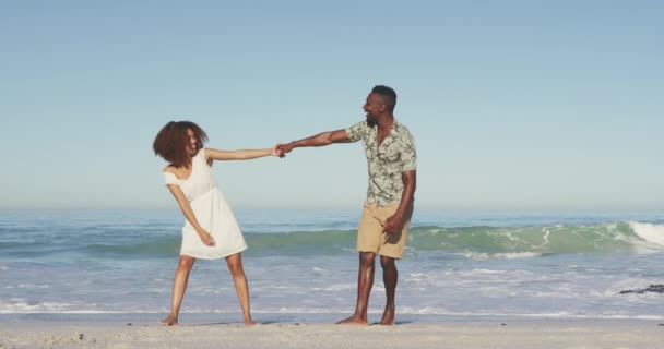 熱帯のビーチで太陽の下で時間を楽しんでいるアフリカ系アメリカ人のカップルのフロントビュー 手を取り合って歩く スローモーションで — ストック動画