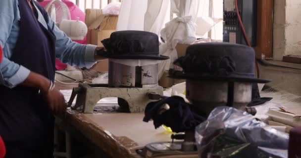 帽子工場で作業場で装置を操作し 帽子工場で帽子を形成するエプロンを身に着けている混合レースの女性の側面図の中央部 前景の材料と背景の装置 — ストック動画