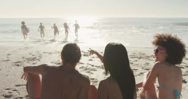熱帯のビーチで太陽の下で時間を楽しんでいる友人の多民族グループの背面ビュー 座って海に歩いて スローモーションで — ストック動画