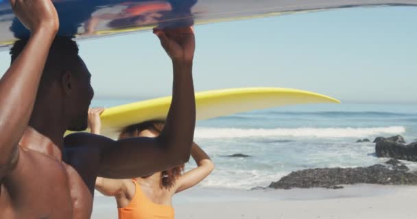 一对非洲裔美国夫妇在热带海滩上享受阳光下的时光 慢吞吞地走着 面带微笑 相互凝视着 拿着冲浪板 — 图库视频影像