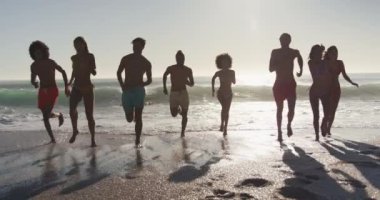 Çok ırklı arkadaş grubunun önden görünüşü. Güneşte güneşli bir plajda vakit geçiriyorlar. Denizden kaçıyorlar.