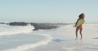 Afrika kökenli Amerikalı bir çiftin tropikal bir plajda güneşin tadını çıkarışını, suya koşuşunu, gülümsemesini ve sörf tahtalarını ağır çekimde taşımasını.