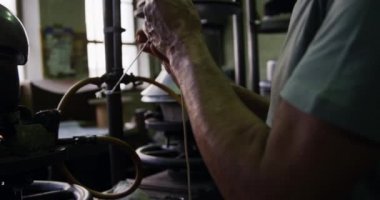 Kıdemli bir melez ırkın orta kesiminde bir ekipman kullanılıyor ve bir şapka fabrikasının atölyesinde iplik kullanılıyor, arka planda ekipmanlar var, yavaş çekimde.