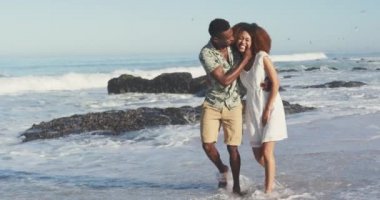 Afrika kökenli Amerikalı bir çiftin tropikal bir plajda güneşlenirken, kucaklaşırken, yürürken ve gülümserken ağır çekimde