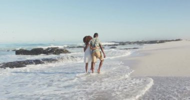 Afrika kökenli Amerikalı bir çiftin, tropik bir plajda güneşin tadını çıkarırken, yavaş çekimde, kucaklaşıp yürürken,