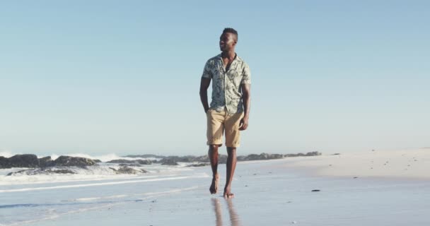 アフリカ系アメリカ人のカップルのフロントビュー熱帯のビーチで太陽の下で時間を楽しんで ポケットに彼の手で歩いて離れて見て スローモーションで — ストック動画