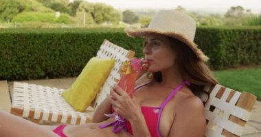 Kafkasyalı bir kadının, havuz başında bir sandalyede oturup, güneşli bir günde, yavaşça gülümseyen, havuz kenarında eğlenirken yan görüntüsü.