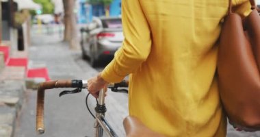 Güneşli bir günde şehirde tesettür takan, sokakta yürüyen ve bisikletini yavaş çekimde süren melez bir kadının arka görüntüsü.
