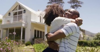 Bahçede eğlenen melez bir çiftin yan görüntüsü. Bir erkek, güneşli bir günde ağır çekimde bir kadını kucağına alıyor.