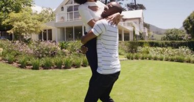 Bahçede eğlenen melez bir çiftin yan görüntüsü. Bir erkek, güneşli bir günde, ağır çekimde bir kadını kucağına alıyor.