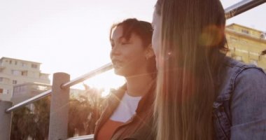 Kafkasyalı ve melez bir kızın yan görüntüsü güneşli bir günde birlikte vakit geçirmekten zevk alıyor, oturuyor, gülümsüyor ve konuşuyor, ağır çekimde..