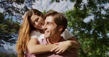 Kafkasyalı bir çiftin yakın çekimde bahçede eğlenirken bir adam, güneşli bir günde, ağır çekimde bir kadını sırtında taşıyor.