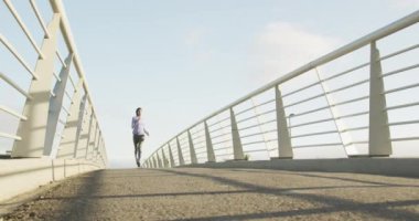 Spor kıyafetleri ve tesettür giyen, güneşli bir günde açık havada mavi gökyüzü ile egzersiz yapan, yavaş çekimde koşan melez bir kadının düşük açılı ön görüntüsü.