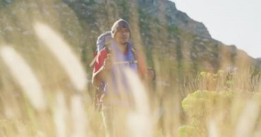 Formda, sakat, protez bacaklı bir ırk adamı, dağlara seyahatinin tadını çıkarıyor, yürüyüş yapıyor, toprak yolda yürüyor, güneşli bir günde, yavaş çekimde, İskandinav bastonları kullanıyor.