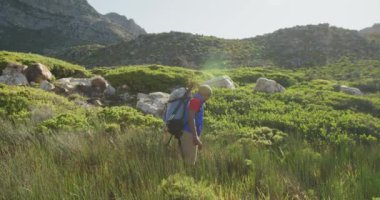Formda, sakat, protez bacaklı bir ırk adamı, dağlara seyahatinin tadını çıkarıyor, yürüyüş yapıyor, toprak yolda yürüyor, güneşli bir günde, ağır çekimde.