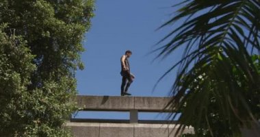 Kafkasyalı bir adam günlük giysiler giyiyor güneşli bir günde şehir sokaklarında parkur yapıyor köprü korkuluklarında ağır çekimde yürüyor..