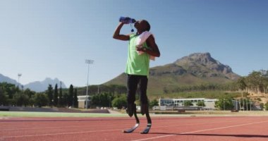 Formda, sakat, protez bacaklı, yarış pistinde duran, suyu yavaş çekimde içen bir ırk adamı.