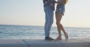 Güneşli bir günde kumsalda beyaz bir çift, birlikte vakit geçiriyorlar, ayakta ve kucaklaşıyorlar, ağır çekimde..