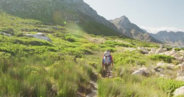Formda, sakat, protez bacaklı bir ırk adamı, dağlara seyahatinin tadını çıkarıyor, yürüyüş yapıyor, toprak yolda yürüyor, güneşli bir günde, ağır çekimde.
