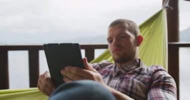 Kafkasyalı bir adam evinde vakit geçiriyor, sosyal uzaklık ve kendini karantinaya alma, kabininin dışındaki bir hamakta uzanıyor, ağır çekimde bir tablet kullanıyor.