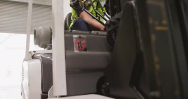 Bir fabrikada çalışan beyaz bir erkek fabrika işçisi, hidrolik ekipman üretiyor, sıkı bir şapka ve yelek giyiyor, ağır çekimde bir depo deposunda forklift kullanıyor..