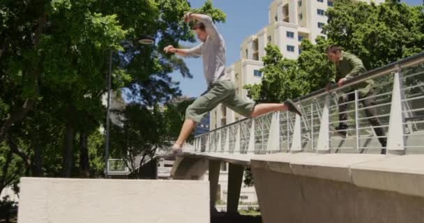 两名身穿休闲装的白人男子 在阳光灿烂的日子里 在城市街道上练习公园 缓缓地跳上桥扶手 — 图库视频影像