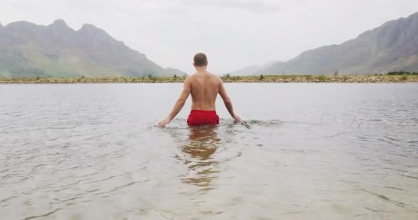 一个白种人 穿着泳裤 慢吞吞地跳进湖里 在登山途中玩得很开心 — 图库视频影像