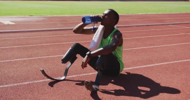 レーストラックに座って水を飲みながら義足の男とフィット 無効混合レースの男 — ストック動画