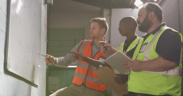 两名白种人和一名非洲裔美国男子在一家生产液压设备的工厂干活 身穿背心 站在白板旁边讨论着 手里拿着一块剪贴板 动作缓慢 — 图库视频影像
