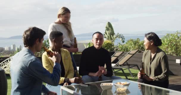 在阴天里 一群多种族的朋友一起坐在屋顶的阳台上 慢吞吞地坐着聊天 喝啤酒 — 图库视频影像
