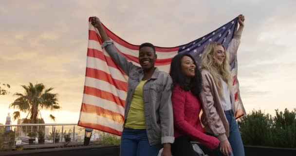 高加索和混合种族的妇女一起挂在屋顶平台上 举着一面美国国旗 慢吞吞地跳着 — 图库视频影像