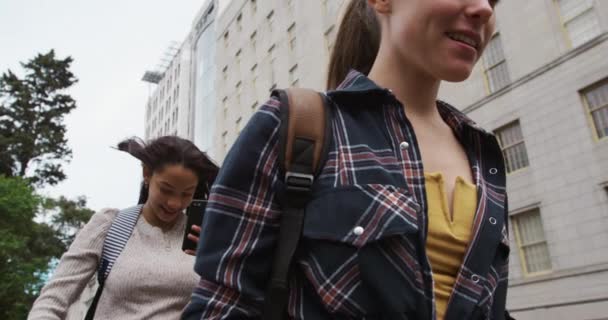 親友同士だ 白人と混じった人種の女の子が晴れた日に一緒に遊び歩き街を歩きスマートフォンを手にスローモーションで — ストック動画
