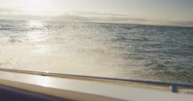 Dalgaların ve güneşin muhteşem görüntüsü denizin dalgalarına yansıyor, hareketli bir tekneden yavaş çekimde kayığın kenarına çarpıyor.