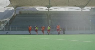 Çim hokeyi oyuncularından oluşan çok ırklı bir grubun ön görüntüsü, maçtan önce antrenman, çim hokeyi sahasında antrenman, güneşli bir günde koşu, yavaş çekim.