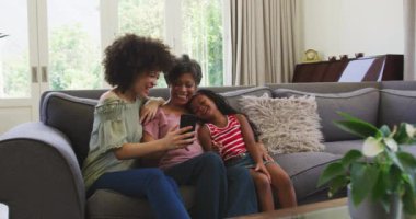 Çok nesildir karışık ırk aileleri evlerinde vakit geçiriyorlar, bir kanepede oturuyorlar, iletişim kuruyorlar, akıllı telefon kullanıyorlar ve gülümsüyorlar, karantinaya alınmış sosyal mesafeler ve kişisel izolasyonlar Coronavirus covid19 salgını sırasında yavaş çekimde