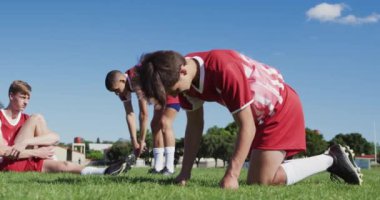 Çok ırklı rugby oyuncularından oluşan genç bir erkek takımının oyun sahasında durup ağır çekimde antrenman yapmaya hazırlanması düşük açılı bir bakış açısı.
