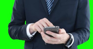 Beyaz gömlekli, takım elbiseli ve kravatlı bir adam, yeşil arka planda akıllı telefonunu kullanıyor..
