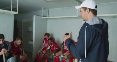 Kafkasyalı bir erkek çim hokeyi koçunun çok ırklı erkek çim hokeyi oyuncularıyla etkileşime girip soyunma odasında oturup yavaş çekimde maçı tartışırken yan görüntüsü.