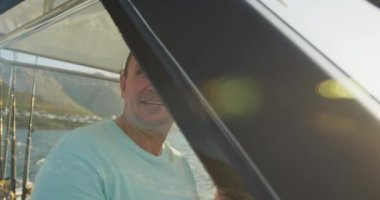 Kafkasyalı bir adam ve genç kızının sahilde güneşlenirken, yavaş çekimde yelkenli sürerken yan görüntüsü.