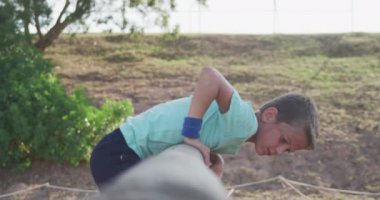 Güneşli bir günde acemi birliğindeki mutlu beyaz bir çocuğun yeşil tişörtlü, ağır çekimde duvardan tırmanması.