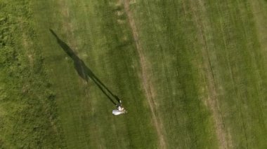 Güneşli bir günde golf sahasında şapkalı ve golf kıyafeti giymiş golf çantası taşıyan bir erkek golfçünün uzaktan kumandalı görüntüsü.