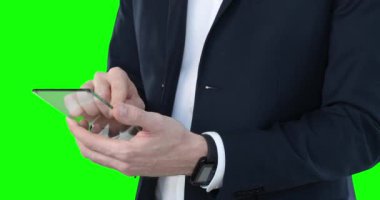Beyaz gömlekli ve takım elbiseli bir adamın orta kısmı yeşil arka planda şeffaf ekran tabletini kullanıyor..