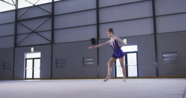 Kafkas kökenli genç bir kadın jimnastikçinin spor salonunda performans sergilerken, bir elinde takla atarken, mor ve beyaz mayo giyerken düşük açılı ön görüntüsü..