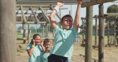 Güneşli bir günde acemi birliğindeki beyaz bir erkek koçun yeşil tişörtlü, yavaş çekimde maymunun yürüdüğü mutlu beyaz erkek ve kız grubunun ön görüntüsü.