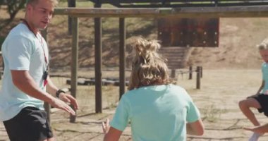 Güneşli bir günde, Acemi Birliğindeki beyaz erkek ve kız çocuklarından oluşan mutlu bir grubun yan görüntüsü. Egzersiz yapıyorlar, zıplıyorlar ve dizlerine dokunuyorlar, hepsi yeşil tişörtler giyiyorlar, yavaş çekimde.