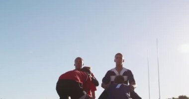 Çok ırklı iki genç rugby takımının takım elbiselerini giyip, bir ragbi maçında ağır çekimde topu yakalamak için iki oyuncuyu kaldırması ön planda.