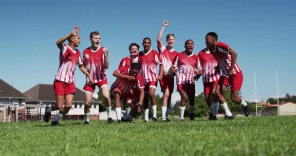 赤と白のチームストリップを身に着けている10代の多民族の男性ラグビー選手のグループのフロントビュー 勝利を祝う 彼らの腕で遊ぶフィールドに提起ジャンプ応援 スローモーションで応援 — ストック動画