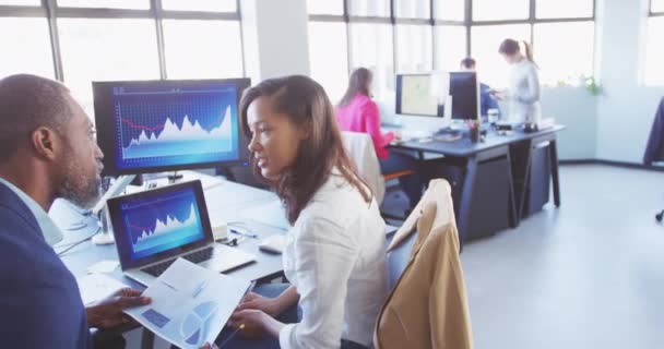 Vue latérale d'une femme métissée et d'un homme d'affaires afro-américain créatifs travaillant ensemble dans un bureau moderne décontracté, utilisant un ordinateur, parlant, se serrant la main, l'homme tenant la paix du papier, avec des collègues en arrière-plan 